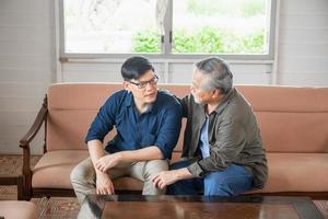 padre asiático mayor da consejos a un hijo adulto en la sala de estar, conceptos familiares de felicidad foto