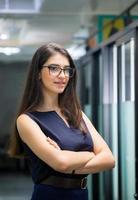 Cheerful young business woman standing with arms crossed in office photo