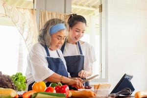 Senior asian mother and middle aged daughter cooking together at kitchen photo