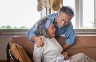 Elderly asian carrying his wife in pain lying on sofa in living room at home, family health care and support concept photo