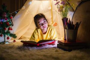 niña leyendo un libro en la tienda, niño feliz jugando en casa, niño divertido y encantador divirtiéndose en la habitación de los niños. foto