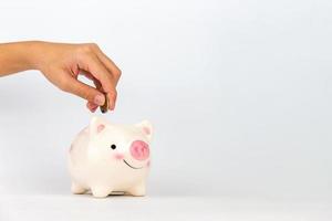 Hand putting coin in piggy bank on white background, Saving concepts photo