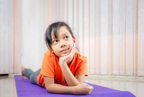 alegre niñita linda sonriendo y pensando en las colchonetas de yoga, concepto de niño feliz foto