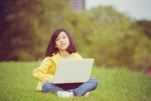 Smiling girl sitting on the grass studying with laptop in the park, Outdoor learning concept photo