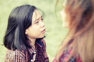 Mother looking at crying daughter, girl crying with tears in park photo