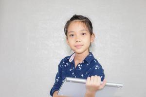 niña pequeña escribiendo en el teclado inalámbrico de la computadora, retrato de un niño feliz mirando la cámara con un fondo borroso foto