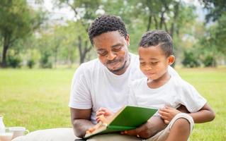 Cheerful african american father and son reading a book, Happy dad and son having a picnic in the park, Happiness family concepts photo