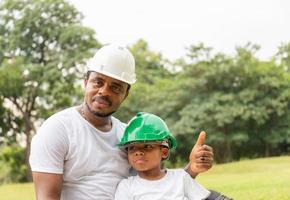 alegre padre afroamericano e hijo con sombrero duro haciendo un picnic en el parque, conceptos familiares de felicidad foto