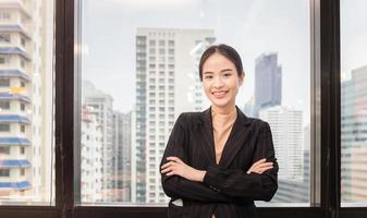 Cheerful young business woman standing with arms crossed in office photo