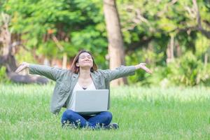 Cheerful woman open arms and sitting on the grass with laptop in the park, Relaxing and Freedom concept photo