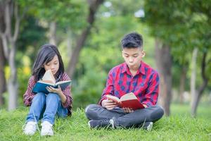 hermano y hermana sentados en el césped y leyendo el libro en el parque, niños jugando al concepto de aprendizaje al aire libre foto