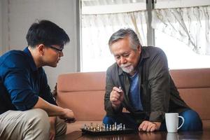 Senior asian father and middle aged son playing chess game in living room, Happiness Asian family concepts photo