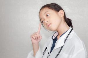 concepto de carrera de ensueño, retrato de un niño pensante con abrigo médico con estetoscopio en un fondo borroso foto