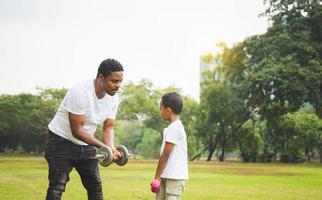 Cheerful african american father and son playing exercising with dumbbell in park, Happiness family concepts photo