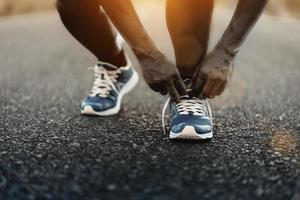 joven corredor afroamericano atándose los cordones de los zapatos en la carretera al aire libre. foto