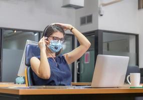 mujer joven telefonista con auriculares con mascarilla de protección contra el coronavirus, equipo ejecutivo de servicio al cliente que trabaja en la oficina foto