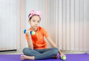 Happy girl doing exercises, kid lifting dumbbells at home, Kids playing concept photo