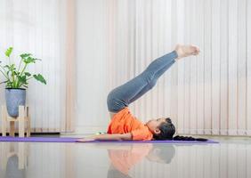 niña feliz y linda practicando yoga en casa, concepto deportivo para niños foto