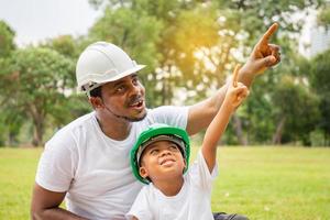 alegre padre afroamericano e hijo con sombrero duro haciendo un picnic en el parque, conceptos familiares de felicidad foto