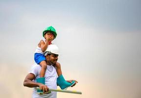 alegre padre afroamericano e hijo con sombrero duro, padre feliz llevando a su hijo sobre los hombros foto