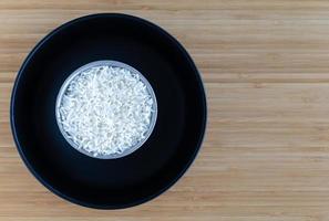 estilo tailandés cocinar arroz al vapor en un tazón pequeño puesto en un plato negro sobre fondo de madera. ángulo de visión superior foto