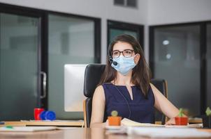 Young woman telephone operator with headset wear protection face mask against coronavirus, Customer service executive team working at office photo