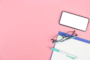 Top view with copy space of smartphone book glasses and pen overhead on pink pastel background, Flat lay and Mock up concept photo