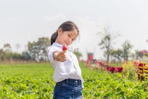 enfoque selectivo de una niña feliz sosteniendo fresas orgánicas rojas frescas en el jardín foto