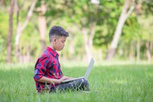 Boy sitting on the grass studying with laptop in the park photo