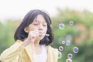 Cheerful a little girl blowing soap bubbles in the park, Kids playing concept photo