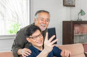 Happy senior asian father and adult son using smart phone talking on video call in living room photo