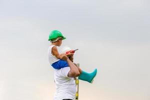 alegre padre afroamericano e hijo con sombrero duro, padre feliz llevando a su hijo sobre los hombros foto