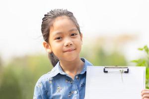 Happy cute little girl holding clipboard checklist with grass flowers in summer day, education concepts. photo