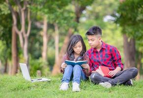 hermano y hermana sentados en el césped y leyendo el libro en el parque, niños jugando al concepto de aprendizaje al aire libre foto