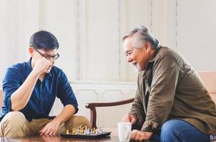 hijo de mediana edad y padre asiático mayor jugando ajedrez en la sala de estar, felicidad conceptos familiares asiáticos foto