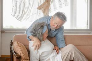 Elderly asian carrying his wife in pain lying on sofa in living room at home, family health care and support concept