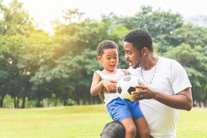 Cheerful african american father and son playing with football in park, Happiness family concepts photo