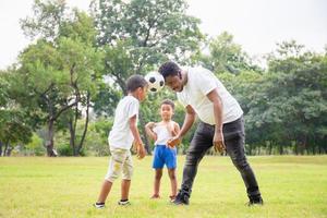 alegre padre afroamericano y dos hijos jugando al fútbol en el parque, conceptos familiares de felicidad foto