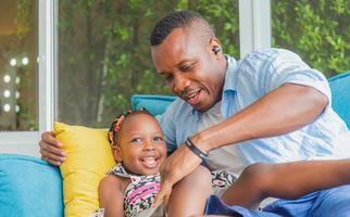 alegre padre afroamericano e hija jugando en la sala de estar, concepto de familia de felicidad foto
