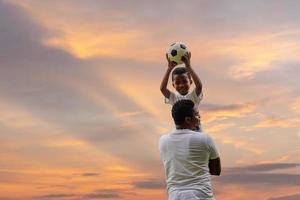 alegre padre afroamericano e hijo jugando al fútbol al aire libre, conceptos familiares de felicidad foto