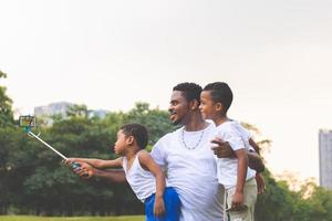 Father with little sons taking selfie picture with smartphone, Cheerful african american father and sons playing in park photo