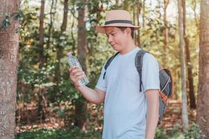 un turista masculino que lleva un bolso, una botella de agua y una cámara camina por el bosque. foto