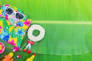 Songkran Festival background with jasmine garland Flowers in a bowl of water, perfume and limestone on a green wet banana leaf background. photo