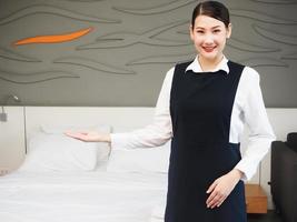 retrato de una atractiva y auténtica sirvienta asiática sonriendo con uniforme de pie con las manos cruzadas y mirando la cámara. concepto de servicio de limpieza foto