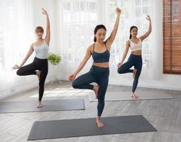 Three attractive beautiful Asian women practice the pose during their yoga class in a gym. Two women practice yoga together. photo