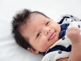 Portrait of three weeks Australian Asian newborn baby or infant lying on the white bed and opening her eyes. photo
