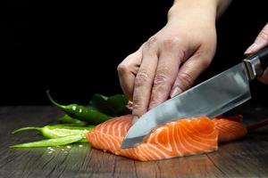 el salmón está en manos del chef japonés y meticulosamente hecho, está usando un cuchillo para cortar el filete de salmón para sashimi y sushi foto