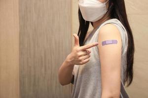 Healthy asian woman concept of recommended inoculation,  Woman holding down her shirt sleeve and showing her arm with bandage after receiving vaccination. photo