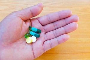 pastillas de colores y medicamentos en la mano sobre la mesa de madera. foto