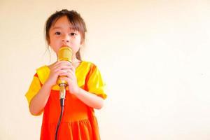 Lovely baby girl wears yellow-orange outfit gokowa outfit or Mugunghwa, and hold gold microphone singing music. Girls and teen fashion dress. photo